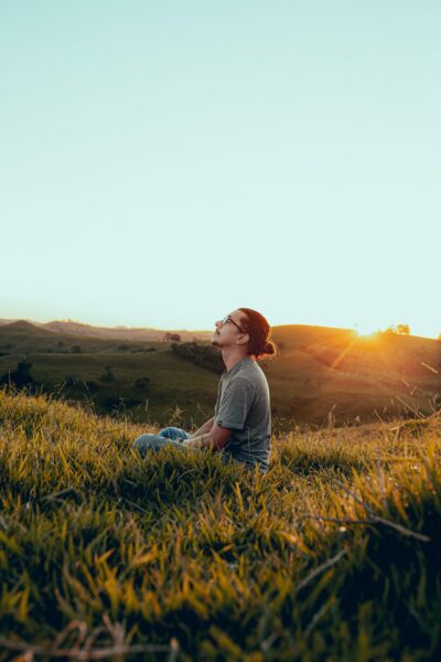 man in white shirt sitting on green grass field during sunset
